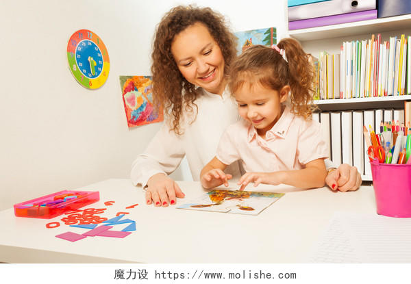 女学生和她的老师在教室的课桌上拼接拼图游戏